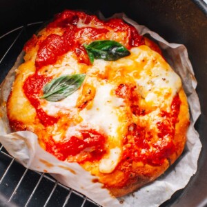 Pizza is cooked with toppings in an air fryer basket.