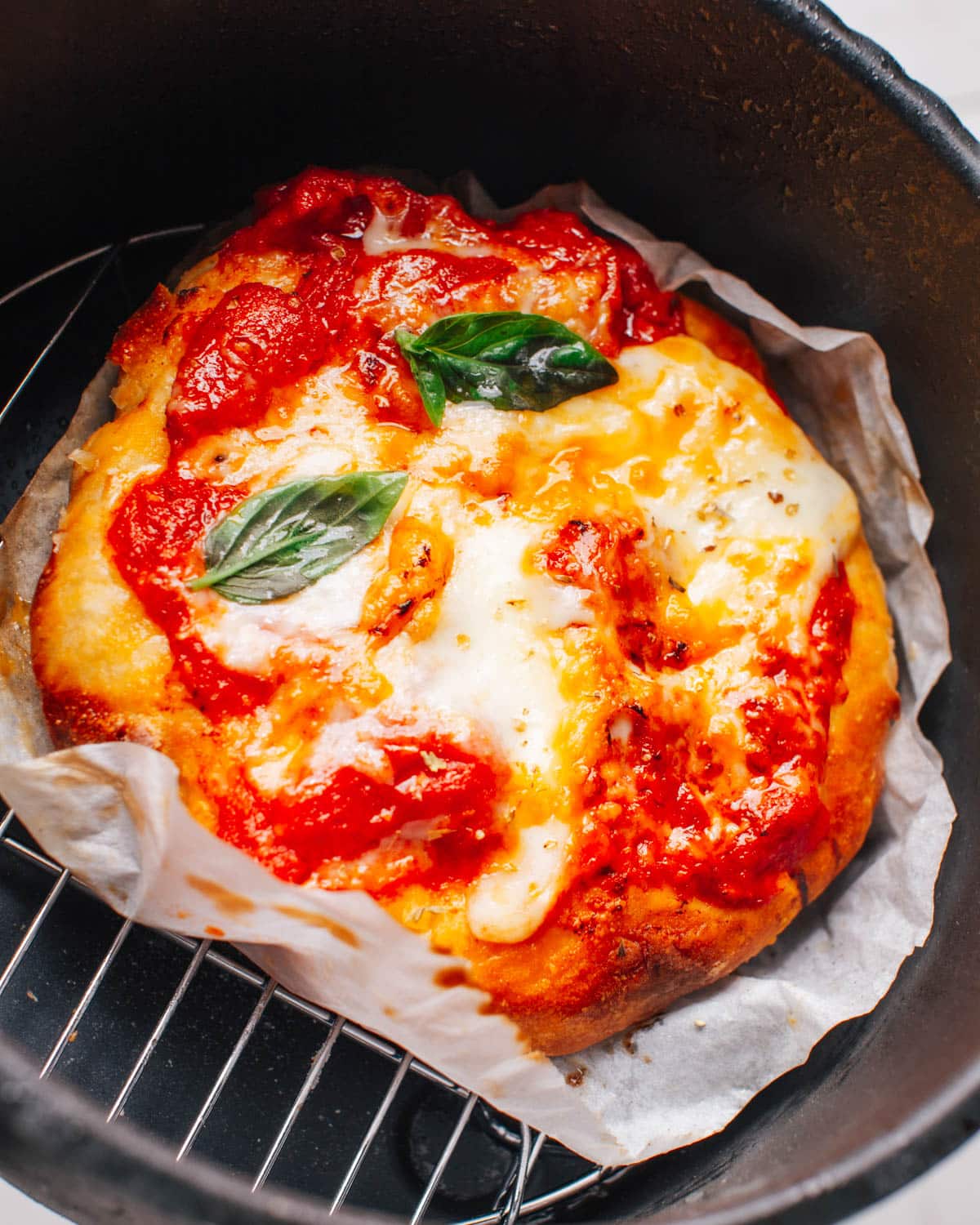 Pizza is cooked with toppings in an air fryer basket.