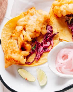 Baja fish tacos artfully presented on parchment paper, drizzled with flavorful Baja sauce and accompanied by a bed of crispy cabbage slaw.