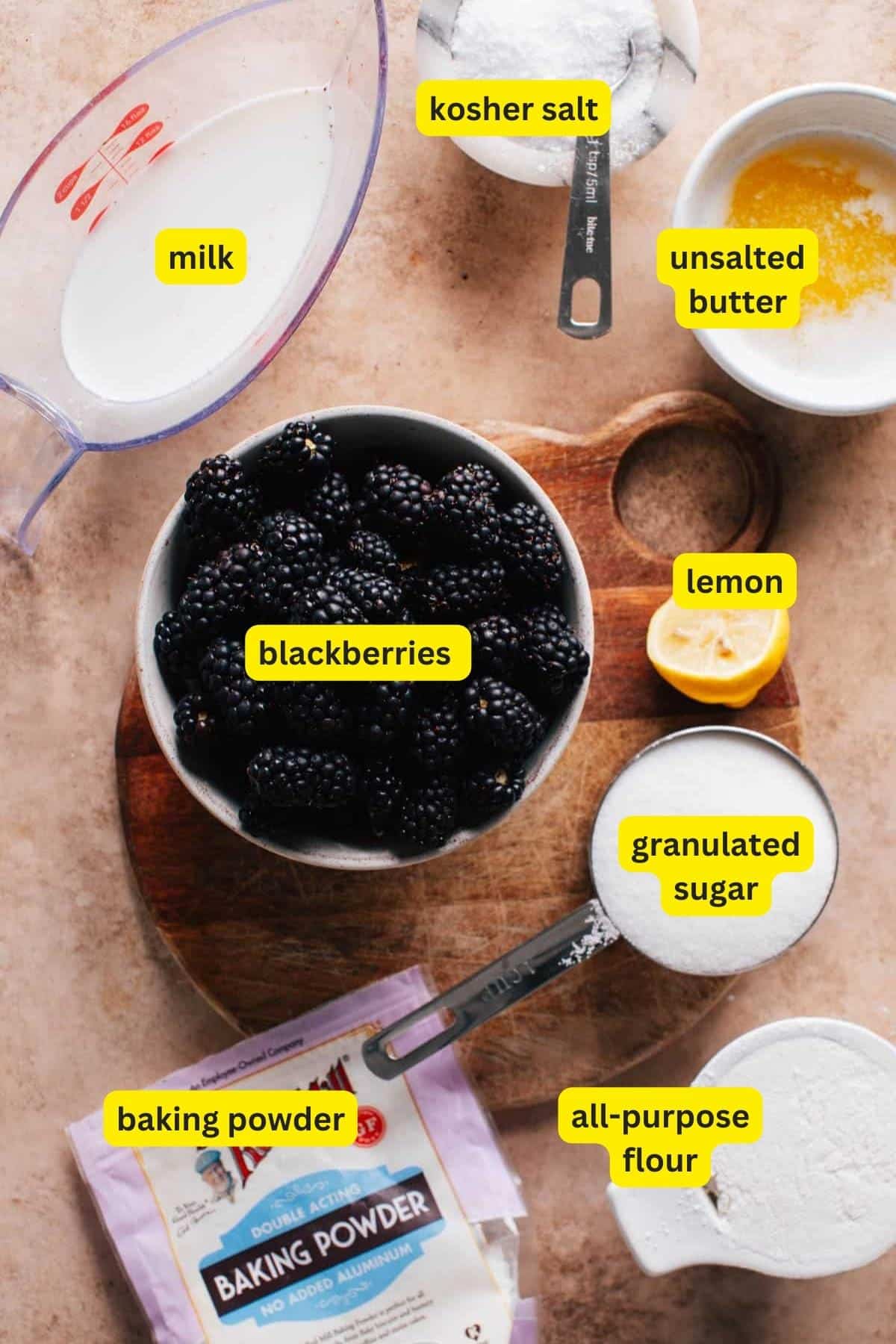 Ingredients for Blackberry Cobbler arranged on a kitchen countertop include blackberries, lemon, milk, granulated sugar, all-purpose flour, baking powder, kosher salt, and unsalted butter