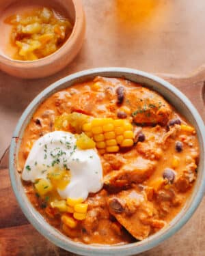 The cream cheese chicken chili is in a bowl and is topped with corn kernels, chilies, and cream cheese.
