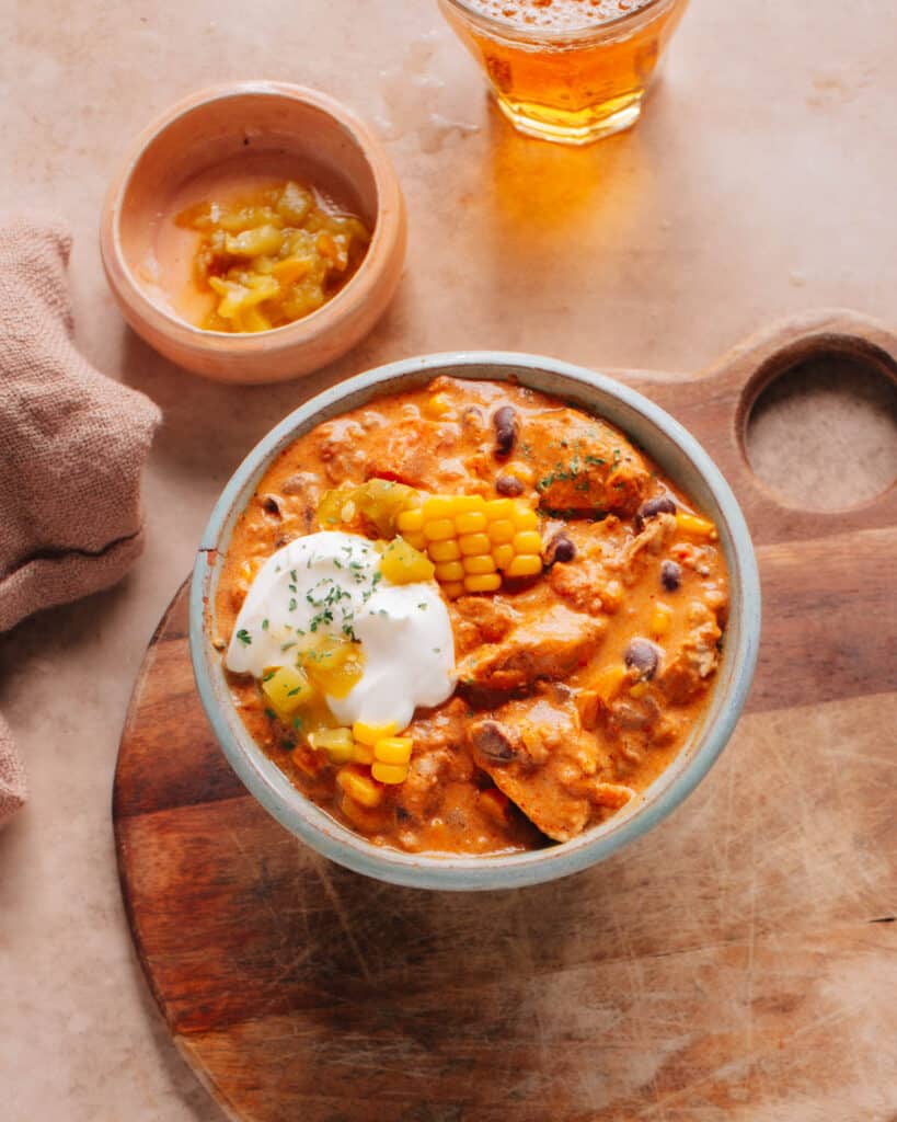 The cream cheese chicken chili is in a bowl and is topped with corn kernels, chilies, and cream cheese.