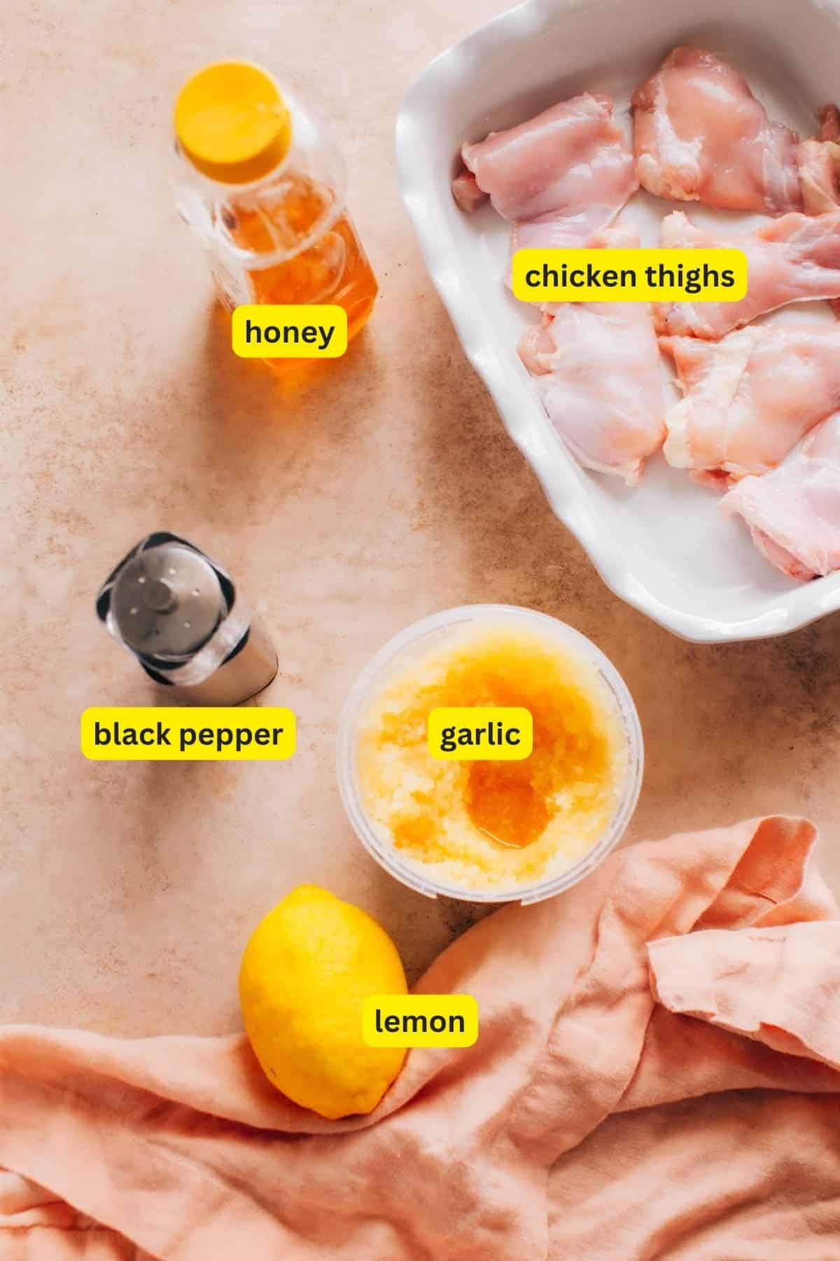 Ingredients for Honey Garlic Lemon Pepper Chicken Thighs laid out on a kitchen countertop, including honey, chicken thighs, black pepper, garlic, and lemon.