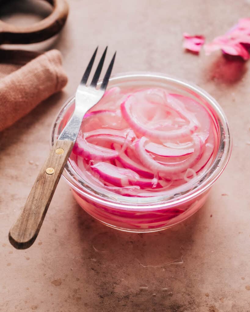 Pickled onions in a small glass bowl with a fork on top.