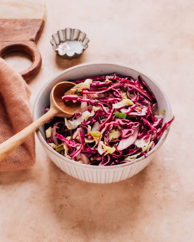 Cabbage slaw for fish tacos in white bowl with wooden spoon