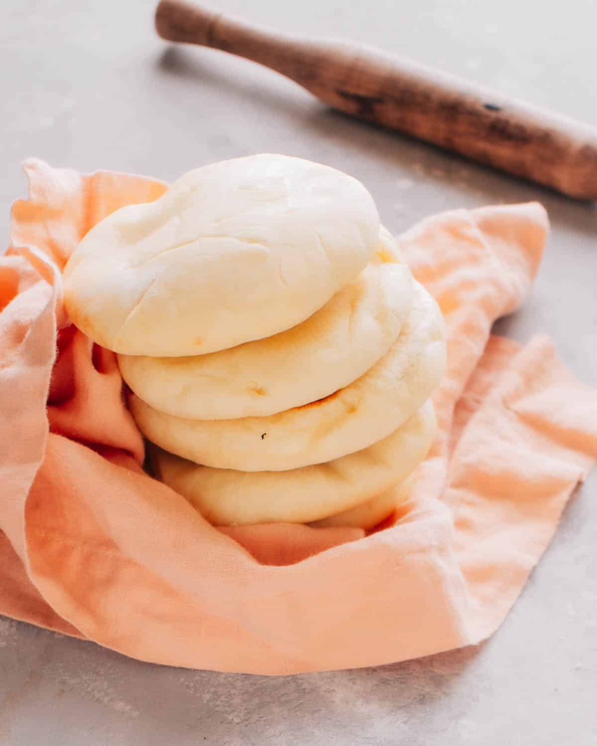 Stack of 4 Turkish breads (bazlama) on a kitchen cloth, with a rolling pin in the background.
