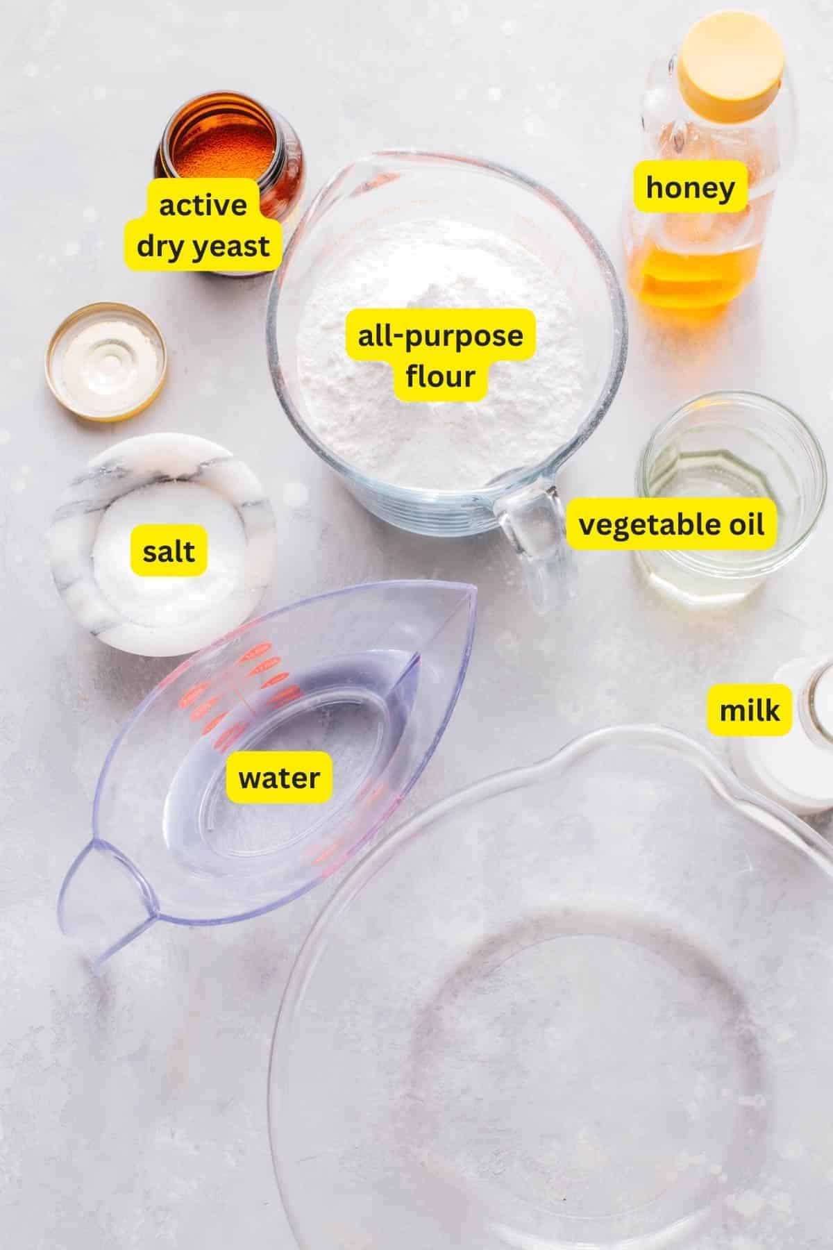 Ingredients for Turkish bread (bazlama) arranged on a kitchen countertop, including active dry yeast, all-purpose flour, honey, salt, water, vegetable oil, and milk.