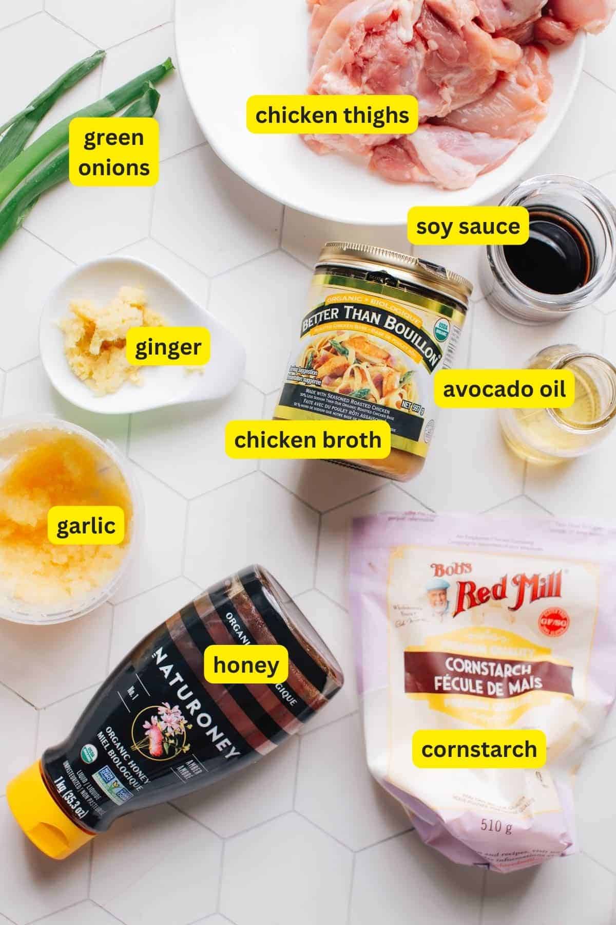 On the kitchen countertop, the ingredients for Garlic Ginger Chicken are laid out, including chicken thighs, garlic, ginger, cornstarch, green onions, honey, soy sauce, chicken broth, and avocado oil.