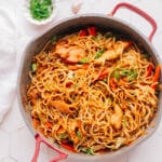 Chicken chow mein noodles in a large skillet, topped with fresh green onions.