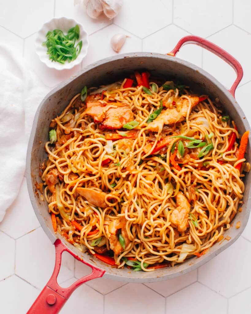 Chicken chow mein noodles in a large skillet, topped with fresh green onions.