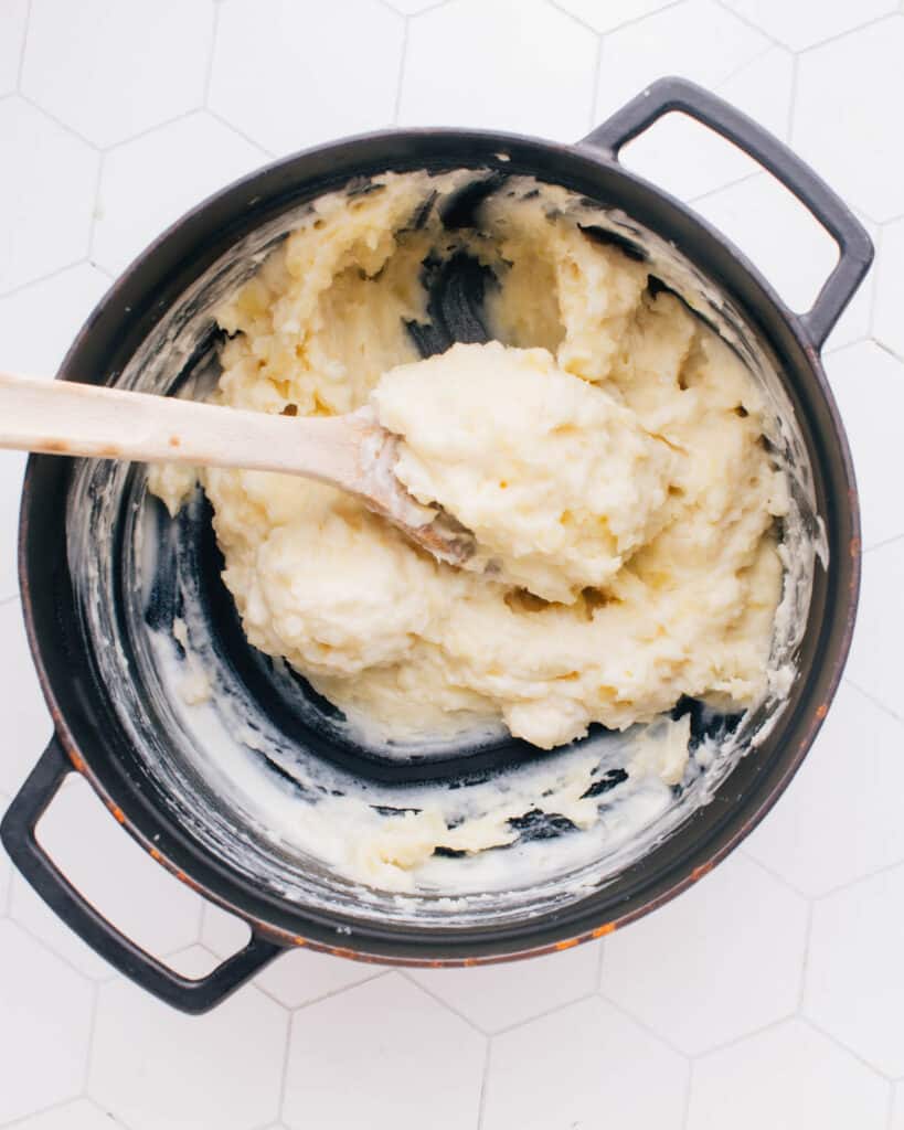 The mashed potatoes are blended with the warm cream and butter mixture, creating a creamy consistency with a spatula.