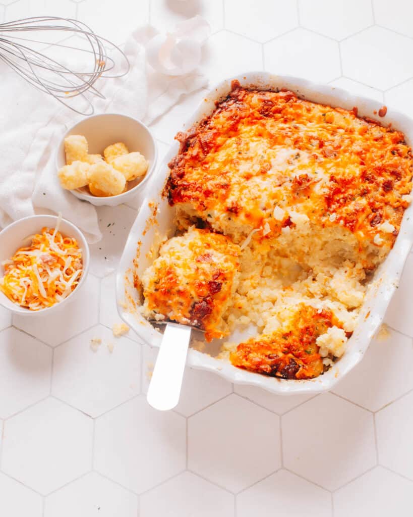 Tater Tot Breakfast Casserole in a baking dish with a serving spoon lifting out a piece.