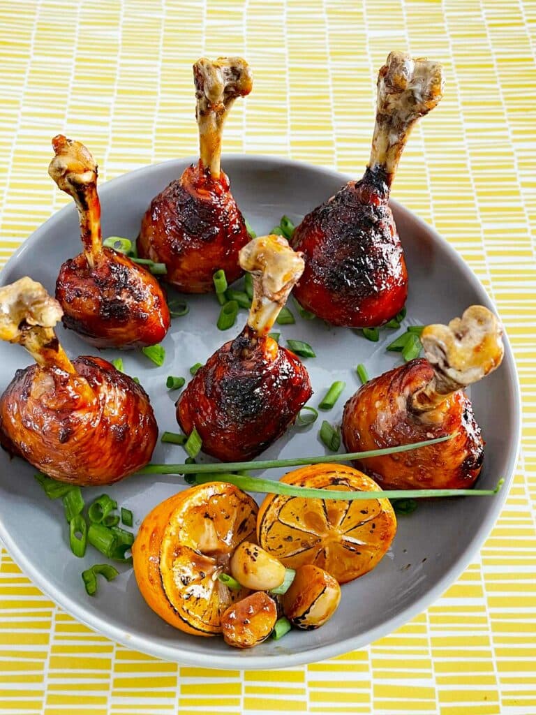 Lollipop Chicken Drumsticks served on a plate with lime wedges and scallions