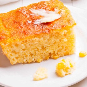 A piece of Cornbread Casserole on a plate with butter.