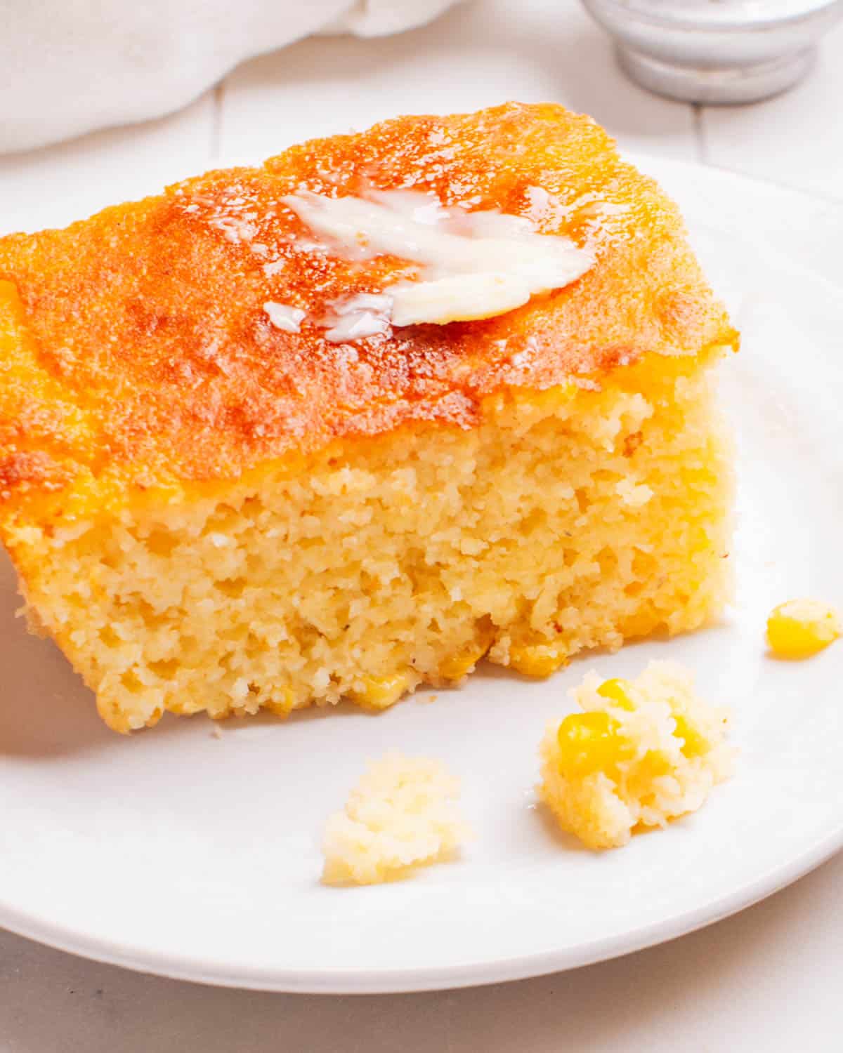 A piece of Cornbread Casserole on a plate with butter.