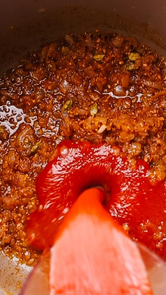 Adding tomato puree to malai kofta sauce.