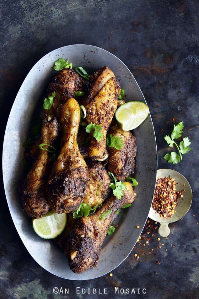 Jamaican Jerk Chicken Drumsticks served with sliced lime wedges and chili flakes