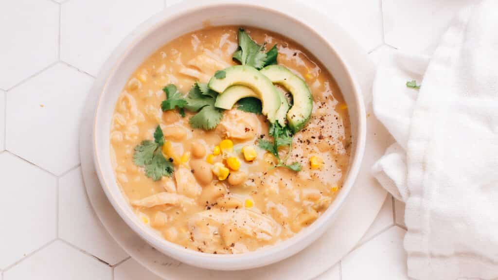 Creamy white chicken chili in a white bowl topped with sliced avacados and cilantro.