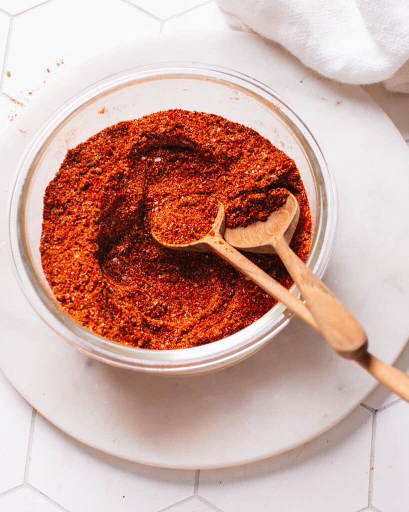 Homemade chili seasoning in a glass container with spoons.