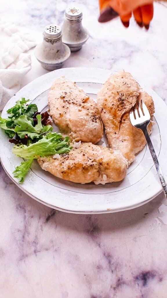 sprinkling seasoning on chicken breast