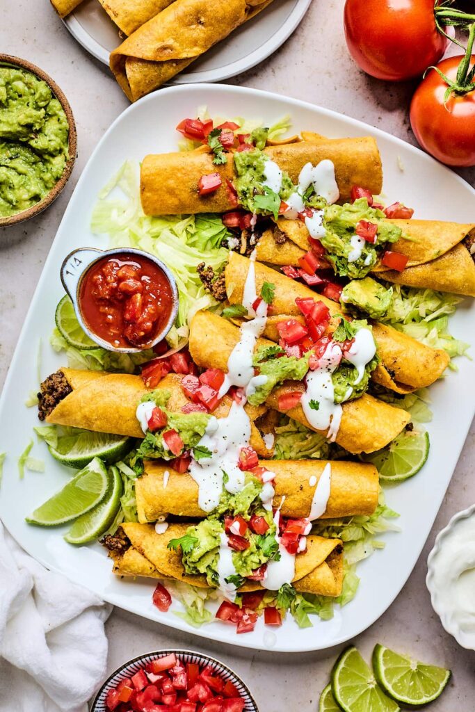 Crunchy taquitos plated with sour cream and salsa