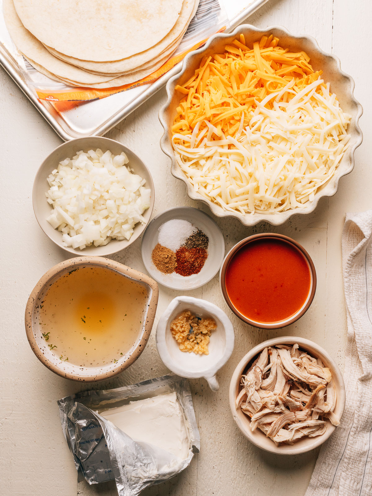 Ingredients for cream cheese chicken enchiladas including shredded chicken, cream cheese, tortillas, cheese, broth, enchilada sauce, onion, garlic, and spices.