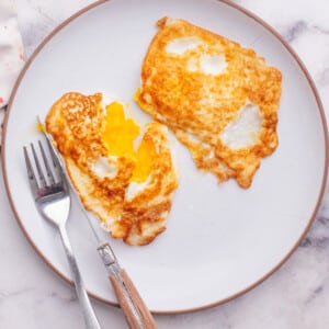 Eggs over medium on a plate with knife and fork.