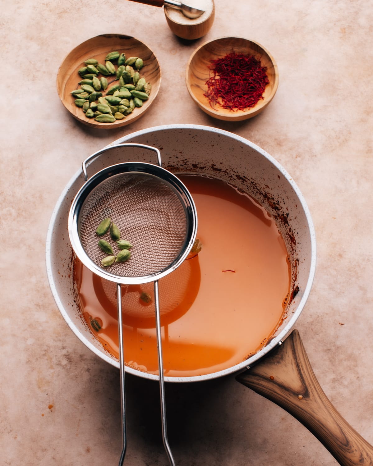 Straining karak chai in a saucepan with a small sieve. 