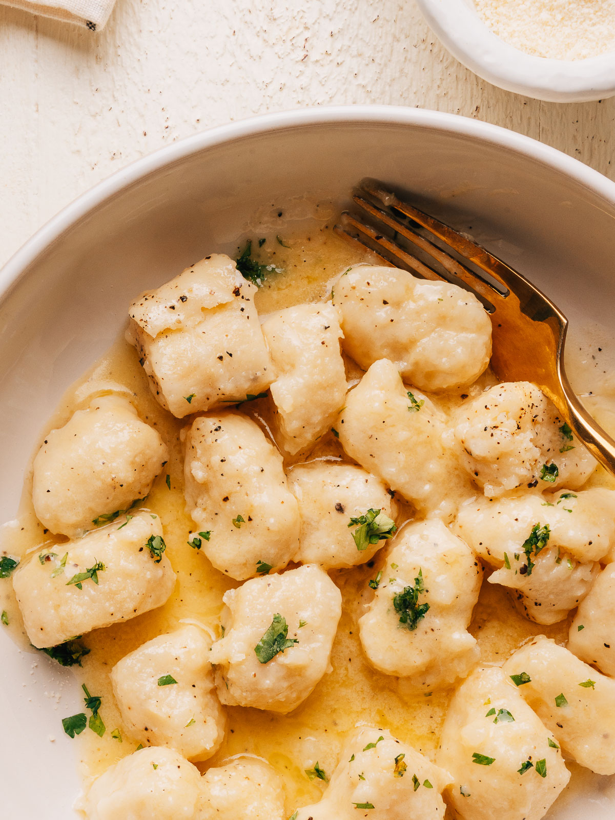 Close up of potato gnocchi tossed in butter sauce with fresh parsley and black pepper.