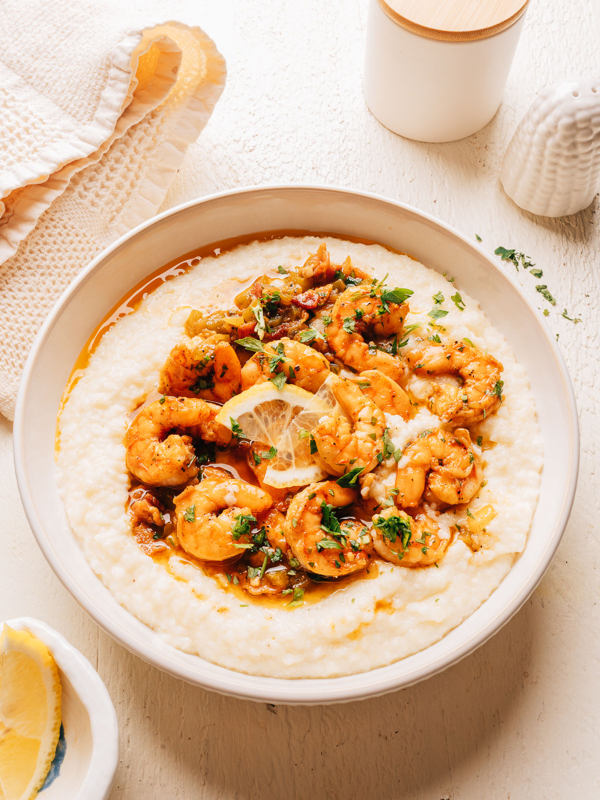 Overhead view of a white bowl of Southern shrimp and grits with parsley and a linen napkin.