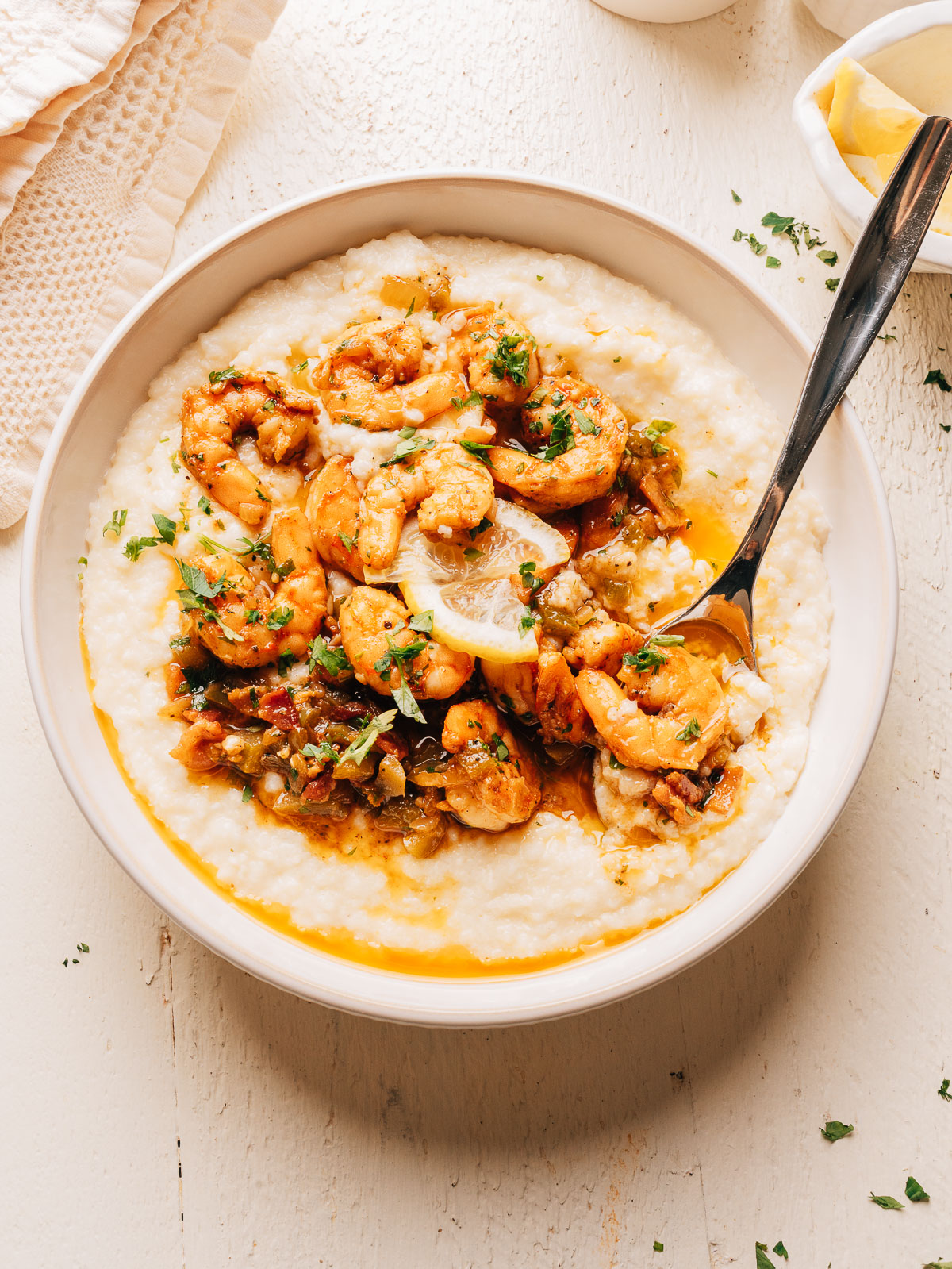 A bowl of creamy shrimp and grits with a spoon and a small dish of lemon wedges.