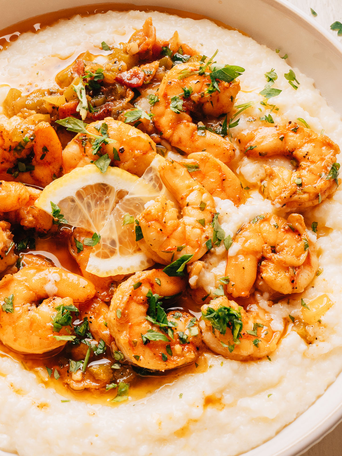 Close-up of shrimp in a smoky bacon sauce over white cheddar grits with fresh parsley.