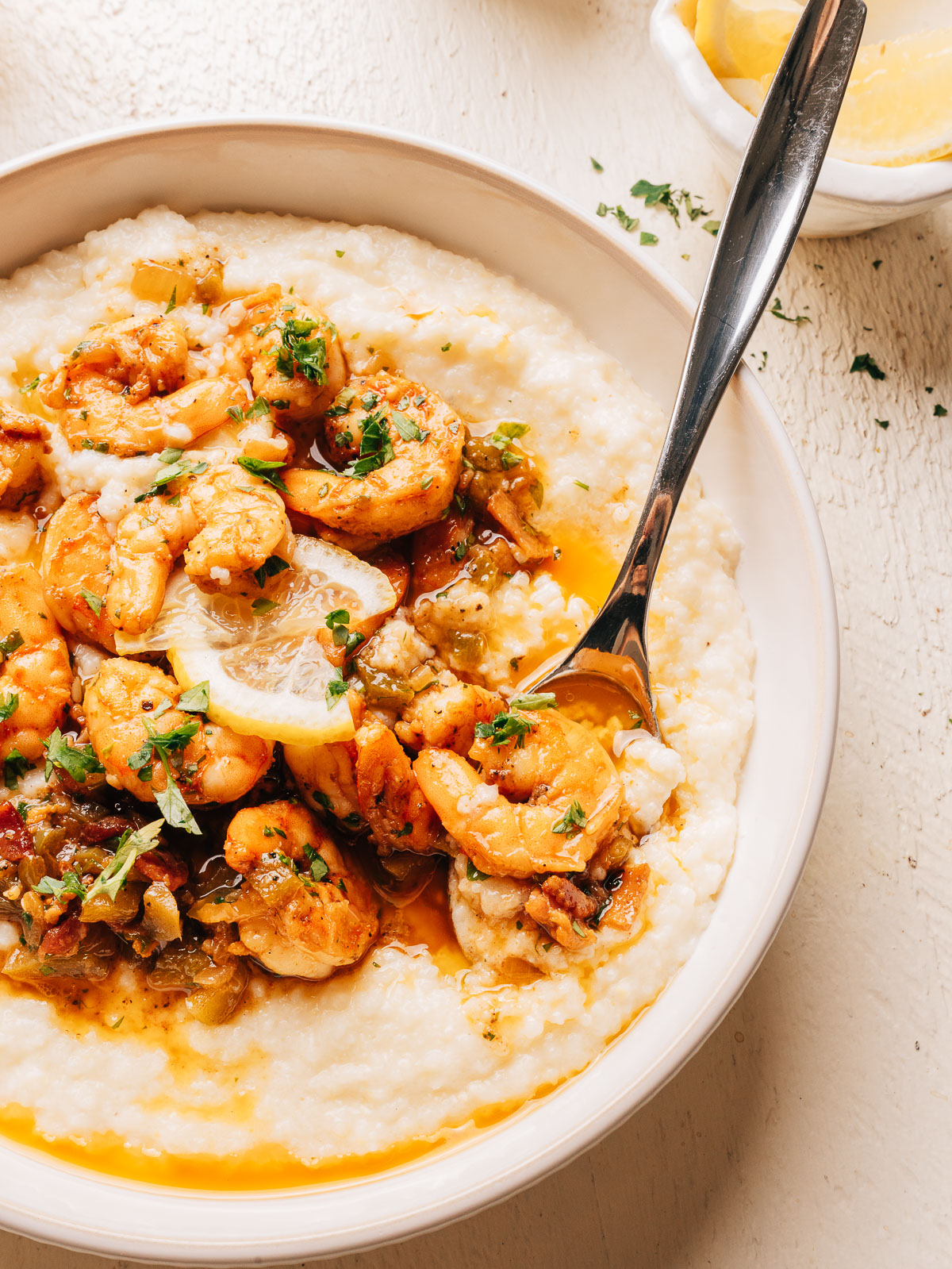 A bowl of shrimp and grits with seasoned shrimp, a bacon pan sauce, and a lemon slice over creamy cheesy grits.