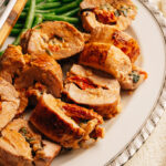 Sliced stuffed pork tenderloin showing creamy sun-dried tomato and spinach filling.