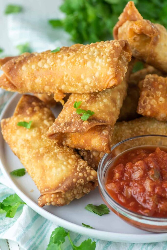 Crunchy egg rolls stacked on a plate with a dip