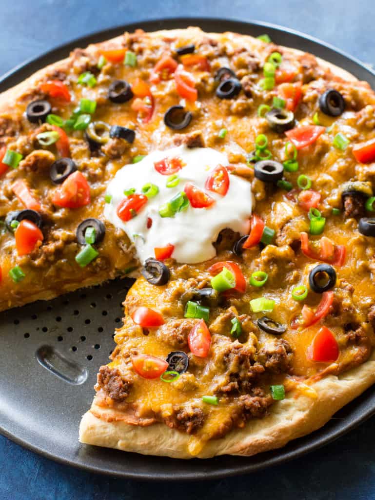 Taco meat pizza topped with a dollop of sour cream and fresh veggies