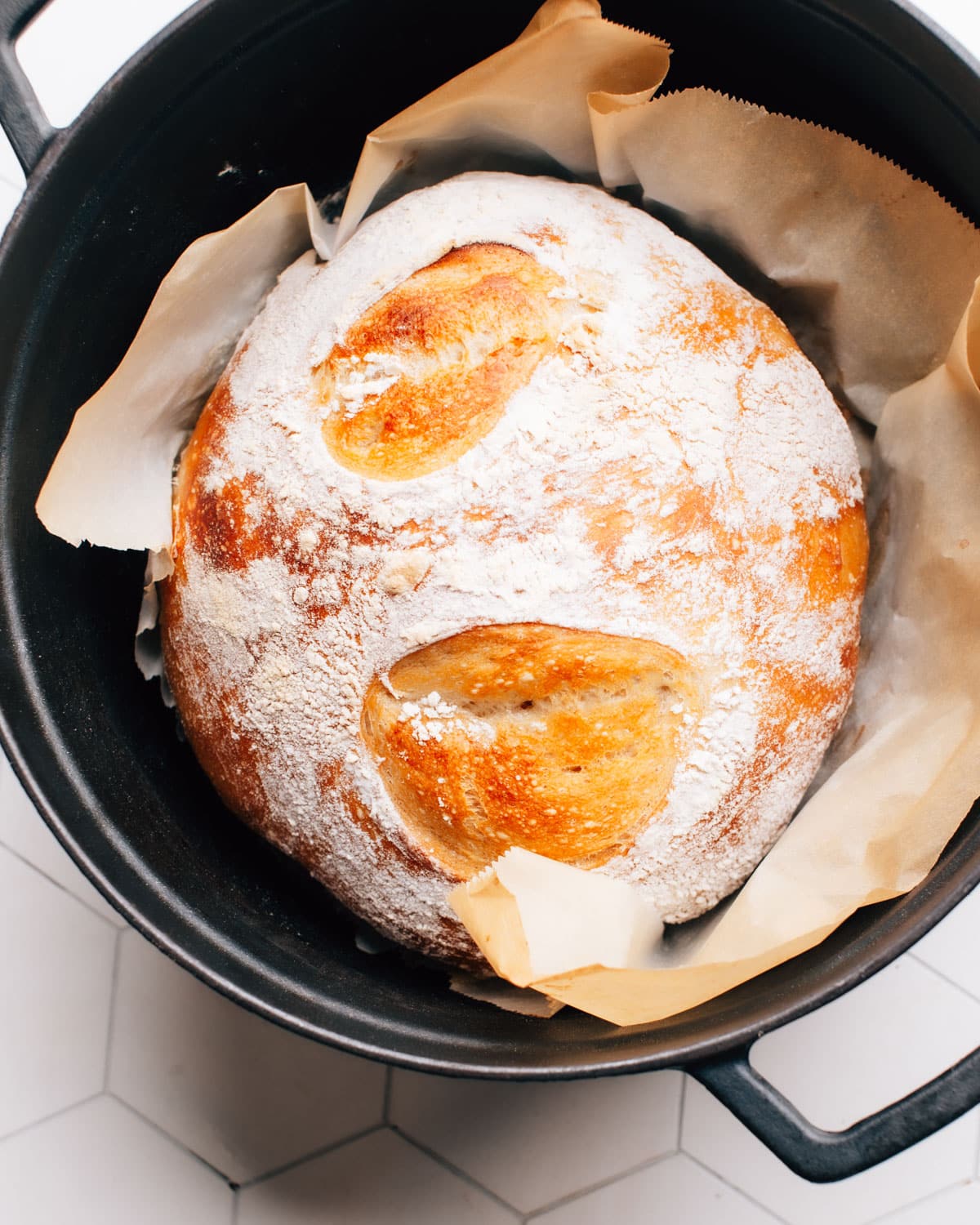 A loaf of no knead bread in a dutch oven with parchment paper.