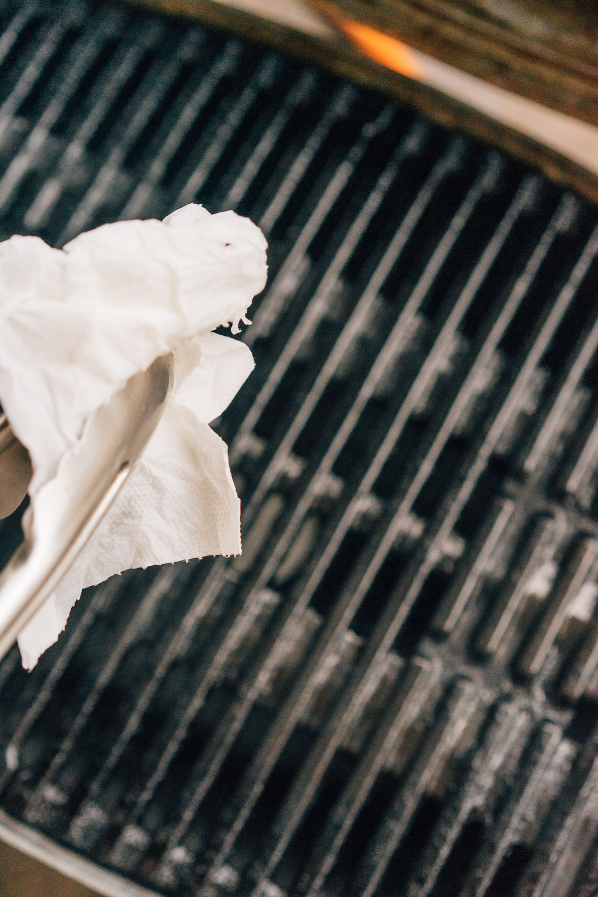 Oiling grill grates with paper towel and tongs. 