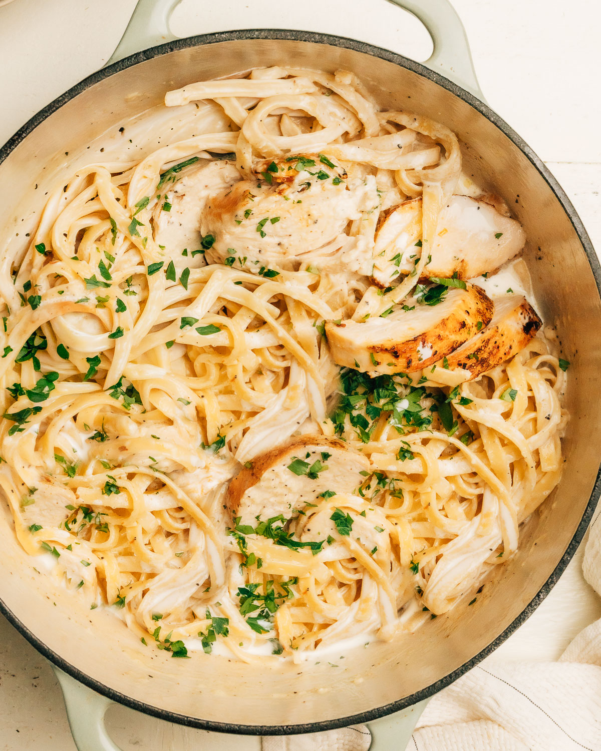 Close up of creamy chicken Alfredo showing fettuccine coated in parmesan sauce and garnished.