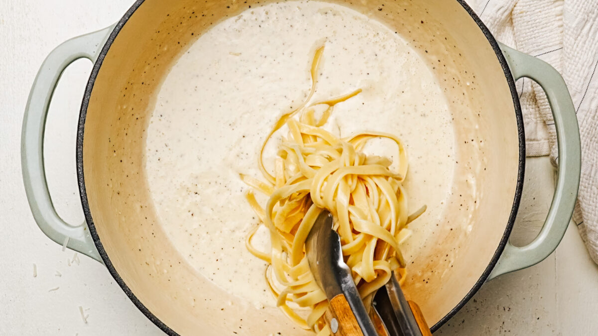 Tossing cooked fettuccine in creamy Alfredo Sauce.
