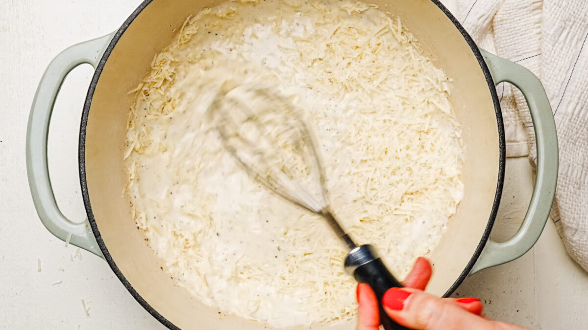 Whisking parmesan cheese into cream sauce to make alfredo sauce.