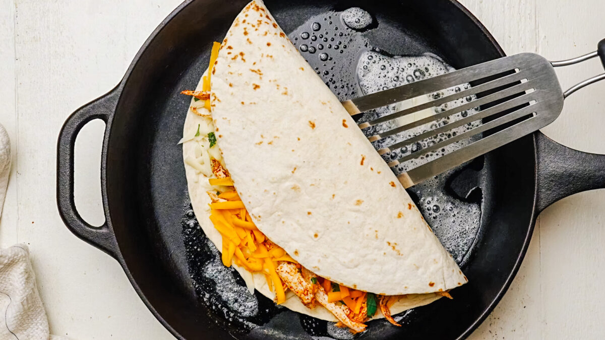 Chicken quesadilla being cooked in a little bit of butter on a skillet until golden brown on the outside. 