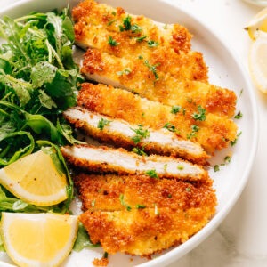 Finished photo of homemade Chicken Schnitzel recipe shown on a plate a with a salad.