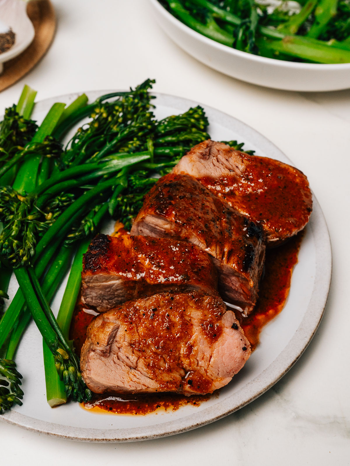 Pork tenderloin marinade on finished pork tenderloin slices with broccolini on a plate.