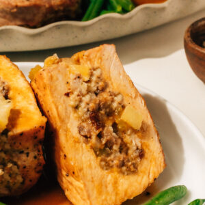 A stuffed pork chop on a plate, cut open to reveal the filling, with more stuffed pork chops in the background.