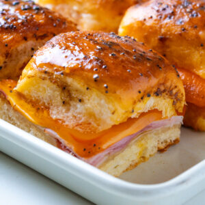 Close-up of a single ham and cheese slider with melted cheese pulling down the side.