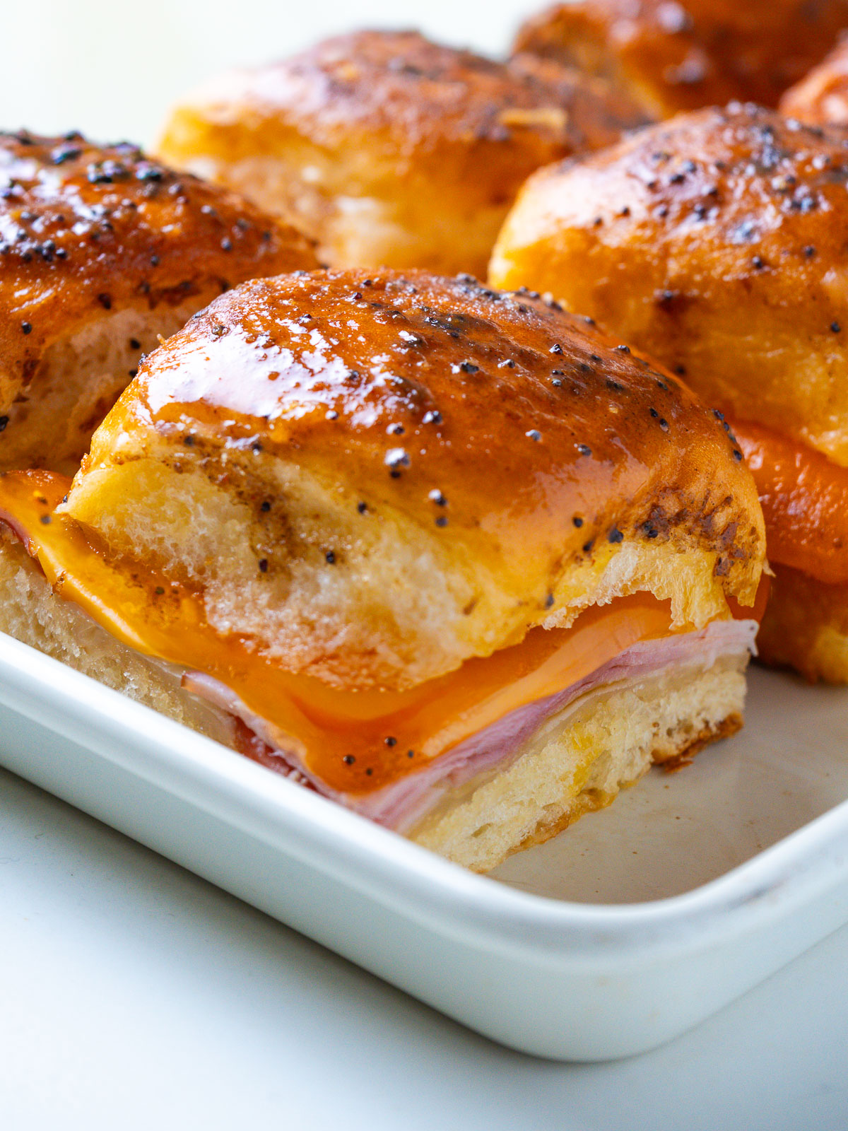 Close-up of a single Hawaiian ham and cheese slider with melted Swiss cheese pulling down the side.