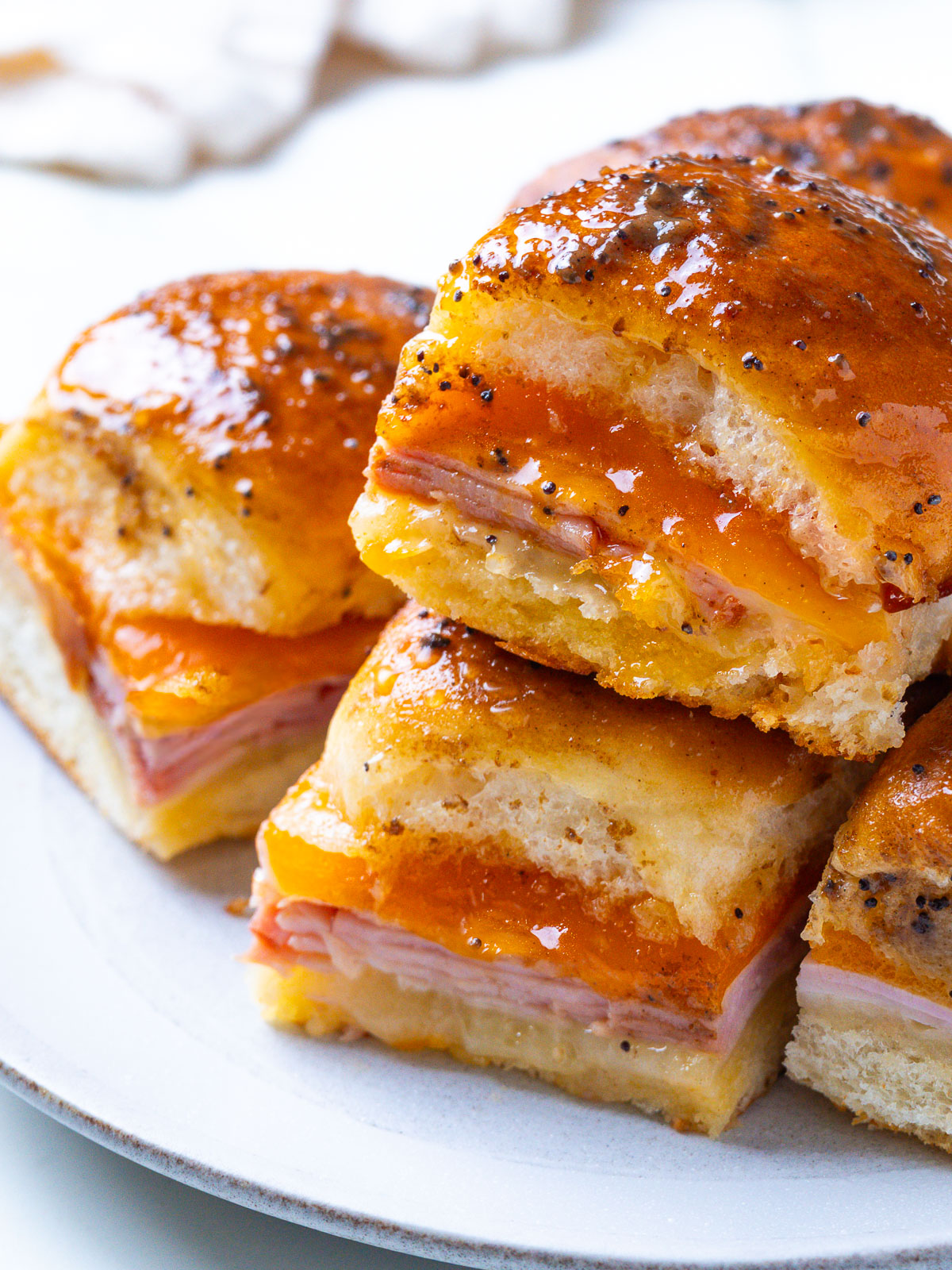 A plate of stacked Hawaiian ham and cheese sliders with a glossy, poppy-seed-flecked glaze.