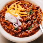 Finisheda Turkey Chili Crockpot Recipe in a bowl with a spoon, sour cream, onions and cheese.