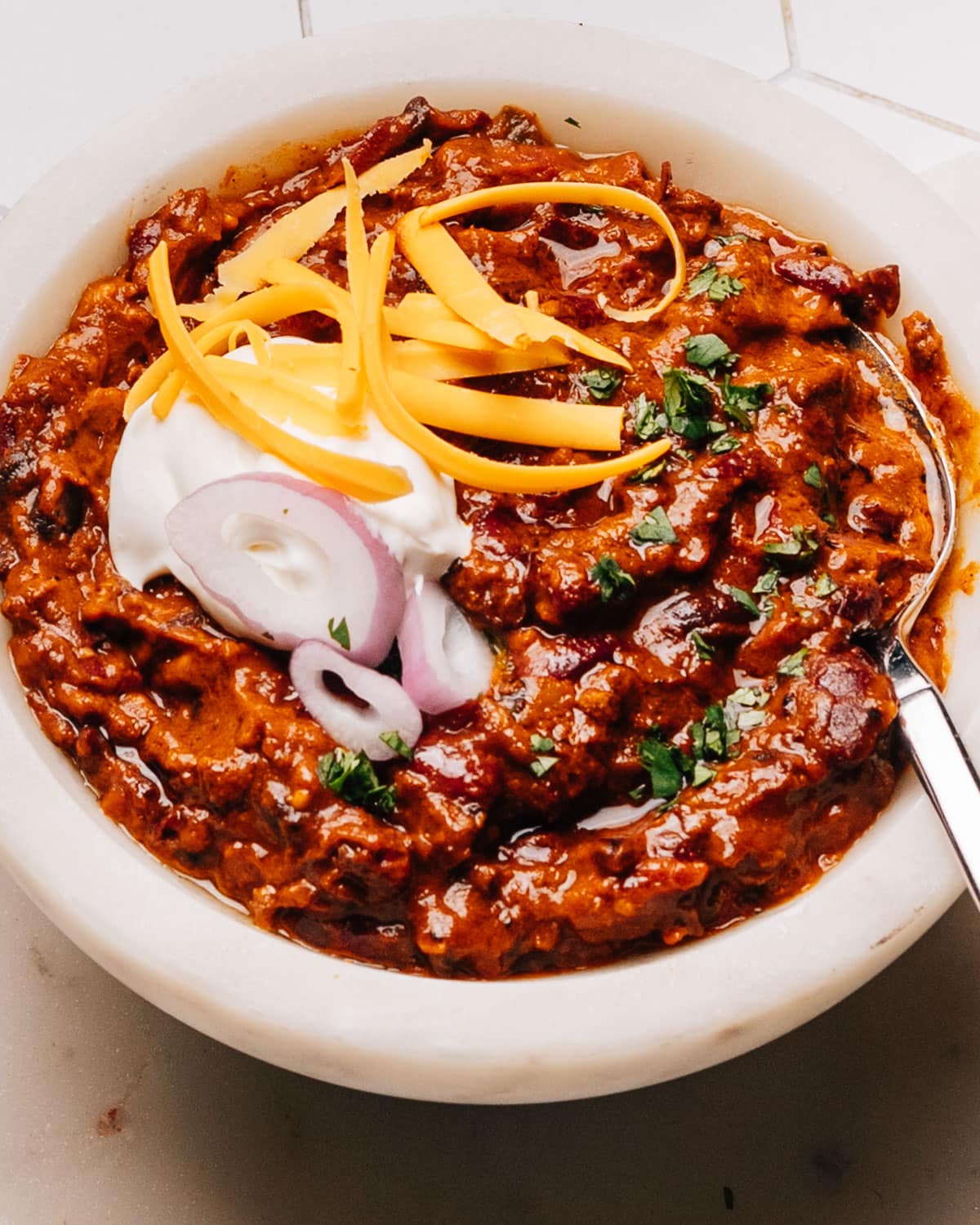 Finished Turkey Chili Crockpot Recipe in a bowl with a spoon, sour cream, onions and cheese.